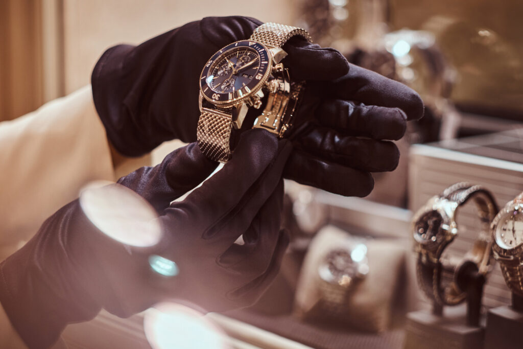 Die Nahaufnahme der Hände des Verkäufers mit Handschuhen zeigt die exklusive Herrenuhr aus der neuen Kollektion im Luxusjuweliergeschäft